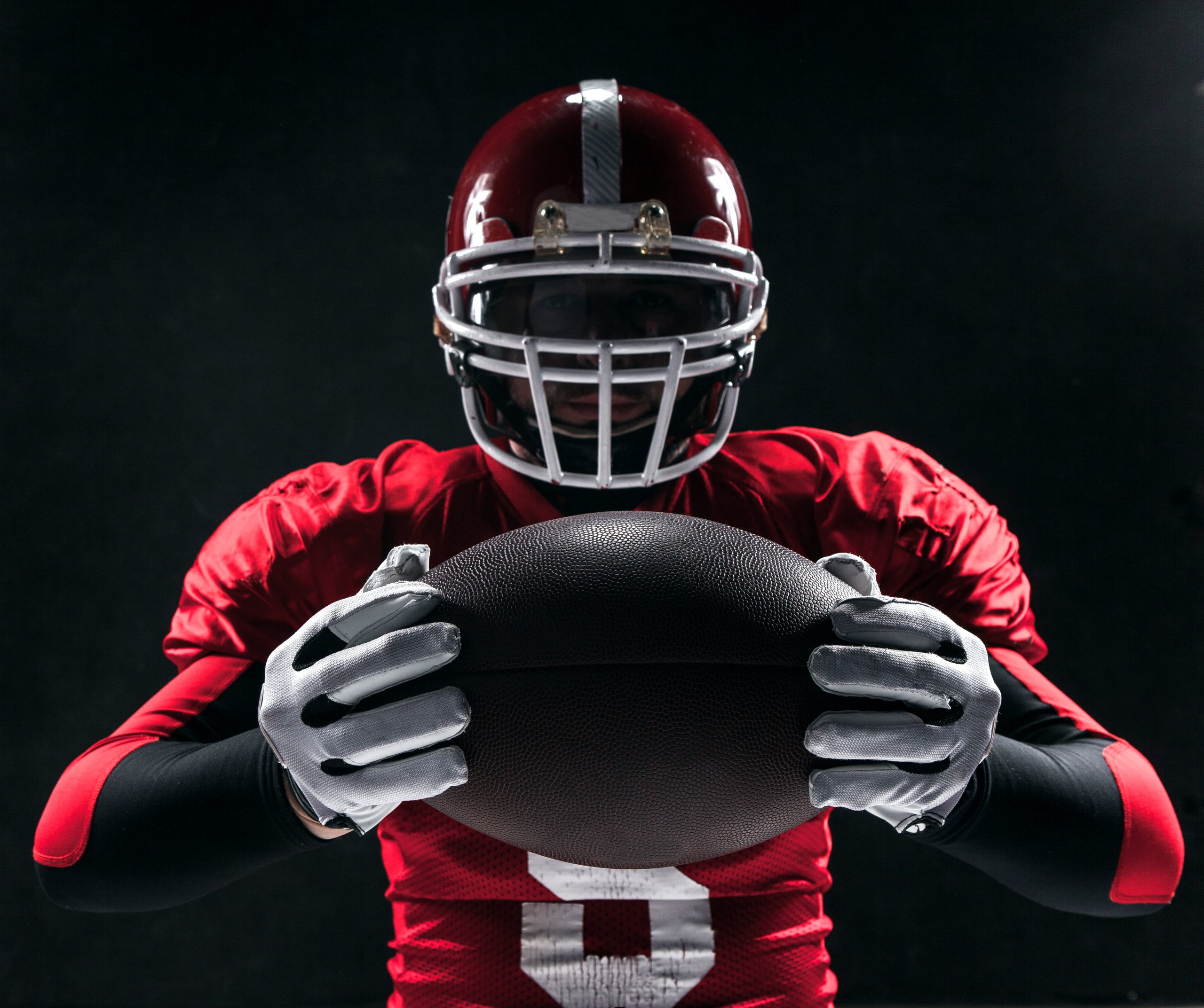 Caucasian fitness man as american football player holding a ball on black background